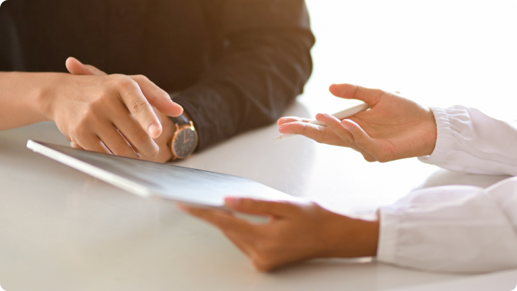 Dois indivÃ­duos sentados a uma mesa, a olhar para o ecrÃ£ de um tablet