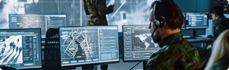 Army personnel engaged in computer work, analysing data on multiple screens in a secure room setting