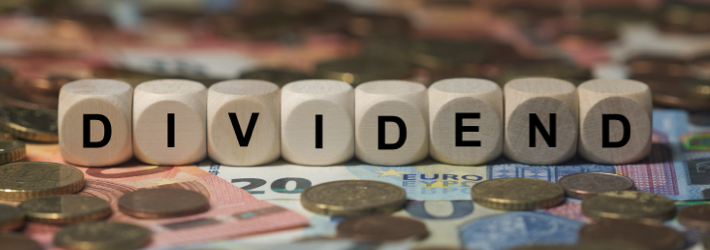 Dinheiro em moedas e notas sobre a mesa, com dados a compor a palavra 'Dividendo'