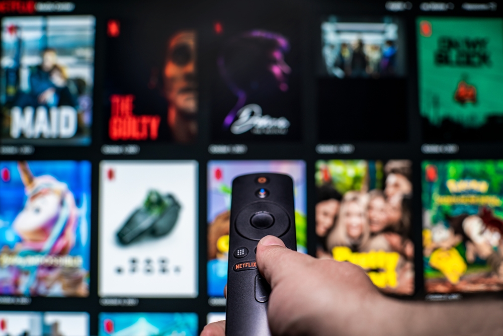Un hombre ve pelÃculas en Netflix. Televisión por internet. La mano humana incluye el control remoto de la pantalla de cine en la imagen borrosa. Televisión.