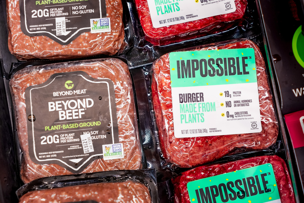 Paquetes de hamburguesas Impossible y Beyond Beef vendidos uno al lado del otro en una tienda Gelson's Markets; ambos productos son de origen vegetal