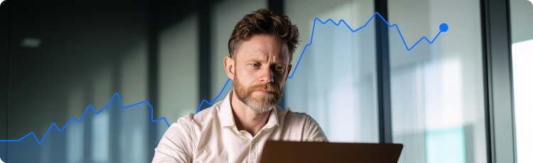 Investidor concentrado a analisar dados financeiros num computador portÃ¡til com um grÃ¡fico de acÃ§Ãµes em ascensÃ£o em segundo plano.