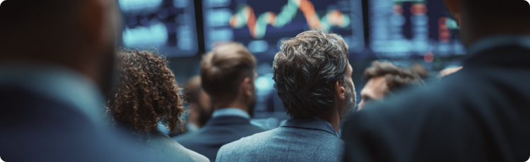 Grupo de traders a observar vÃ¡rios grÃ¡ficos de aÃ§Ãµes e ecrÃ£s de dados financeiros num ambiente movimentado durante a sessÃ£o.