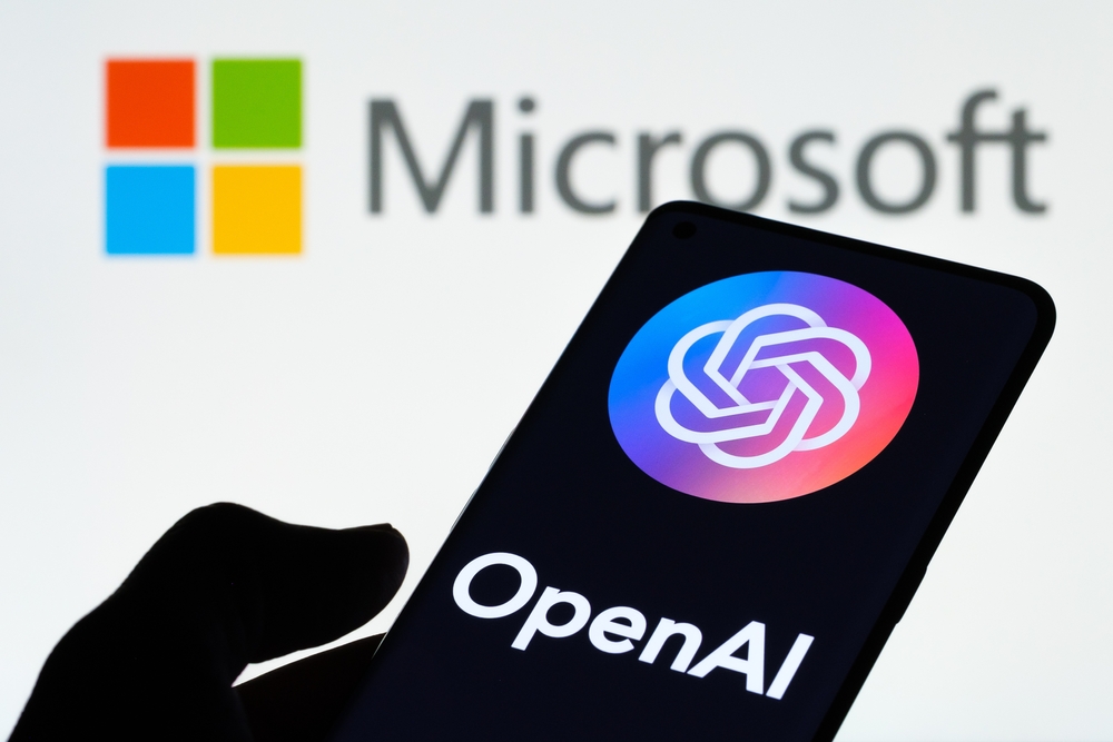 Logo de OPENAI visto en un smartphone con pantalla de mano y portátil con el logotipo de MICROSOFT en segundo plano.