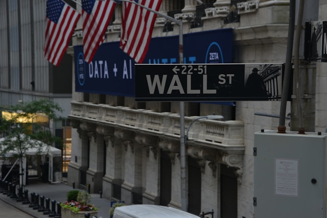Placa de rua a indicar a direÃ§Ã£o da Wall Street com a bandeira dos Estados Unidos ao fundo