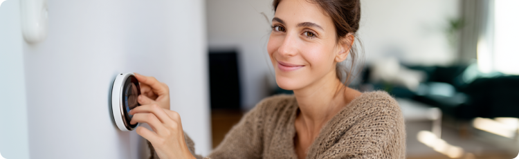 Mulher sorridente ajustando um termostato inteligente em casa, representando eficiÃªncia energÃ©tica, tecnologia moderna de serviÃ§os pÃºblicos e envolvimento do consumidor com serviÃ§os pÃºblicos.