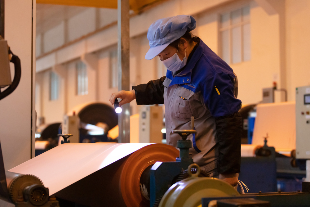 Los trabajadores de una gran empresa de fabricacion de cobre operan maquinaria para producir productos de lamina de cobre.