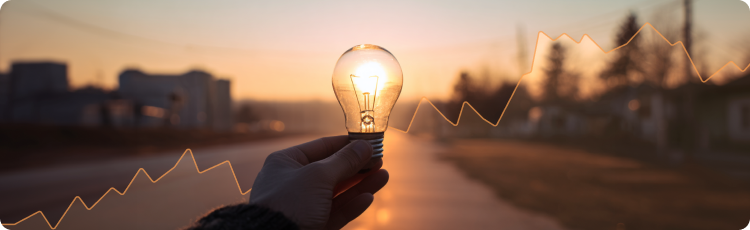  Tangan memegang bola lampu menyala di latar matahari terbenam dengan grafik saham naik di belakangnya melambangkan potensi pertumbuhan dan inovasi dalam investasi saham utilitas.