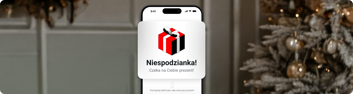 Telefon obrazujÄcy funkcjÄ Podaruj prezent w aplikacji XTB na tle ÅwiÄtecznych dekoracji