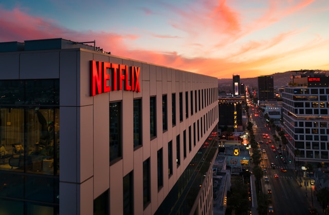 PrÃ©dio com letreiro escrito 'Netflix' em frente Ã  avenida movimentada ao por do sol