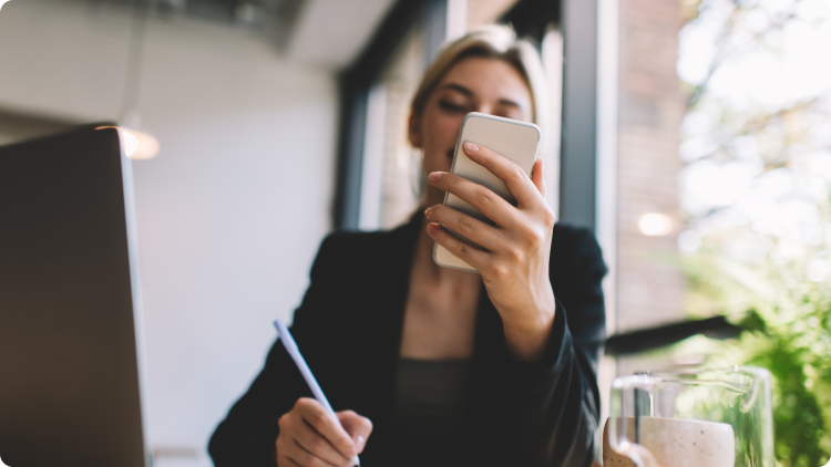 Seorang wanita duduk di meja, menggunakan smartphone-nya untuk mencatat