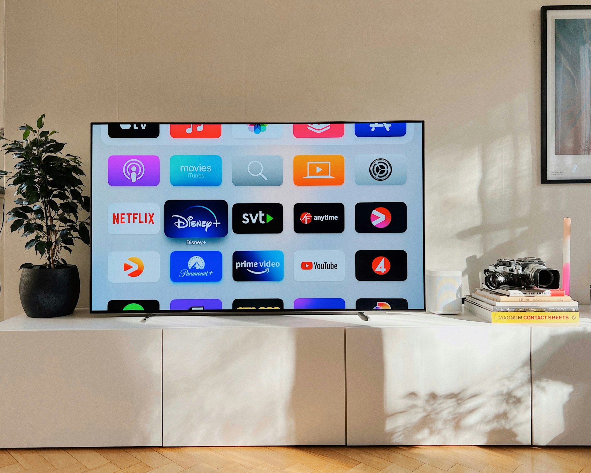 Sala de estar com televisÃ£o ligada em cima de mÃ³vel branco a mostrar diferente aplicaÃ§Ãµes de streaming como a Netflix, Paramount e Apple TV