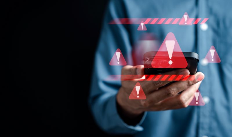 Imagen de una persona con un mÃ³vil del que sale un emoji de alerta en un artÃ­culo sobre las estafas de criptomonedas