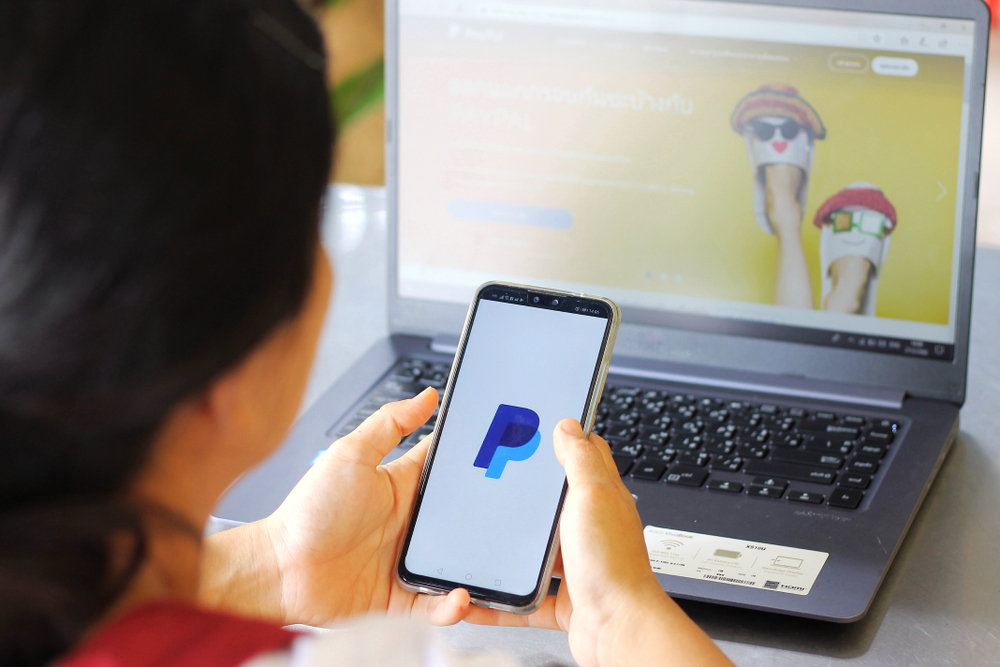 Una mujer mira un telefono con la app de paypal abierta