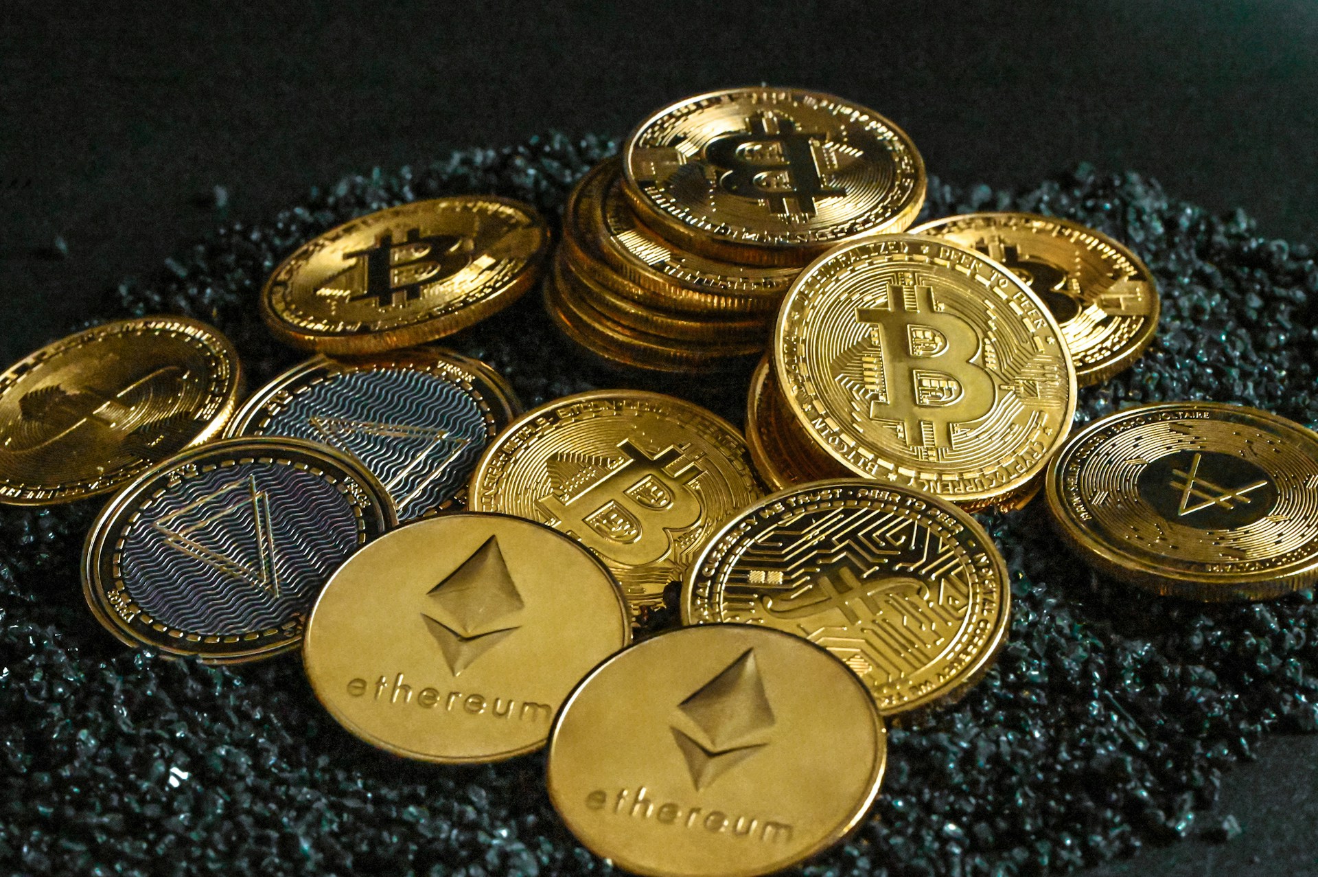 Uma pilha de moedas cripto como Bitcoin e Ethereum em cima de um chÃ£o de cascalho