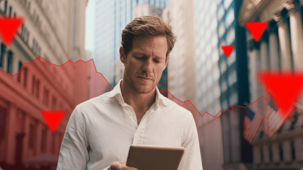 Investidor preocupado segurando um tablet em Wall Street, com um gráfico de ações em queda e sinais de alerta, representando recessões do mercado financeiro e crises económicas.