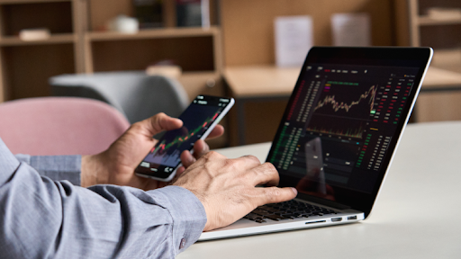 Man holding a phone and laptop with charts
