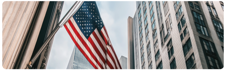 Un drapeau amÃ©ricain flotte devant des gratte-ciel imposants, symbolisant le patriotisme au milieu de lâarchitecture urbaine