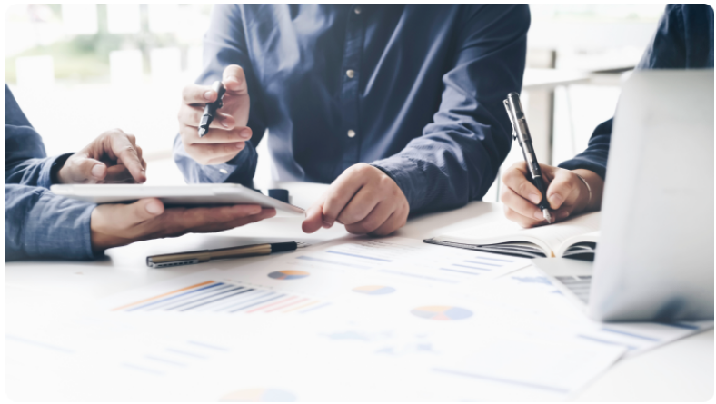 Groupe de trois personnes collaborant Ã  une table avec un ordinateur portable et des documents.